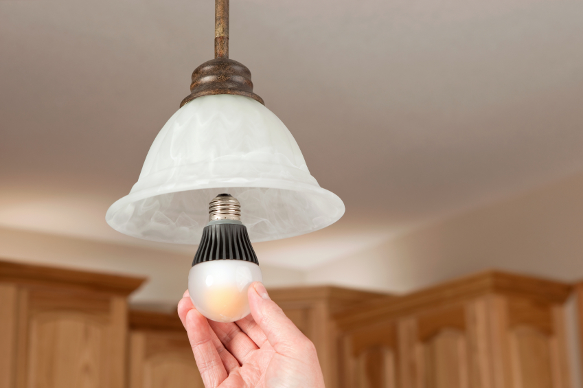 Hand installing or removing a light bulb from a hanging frosted glass ceiling lamp.
